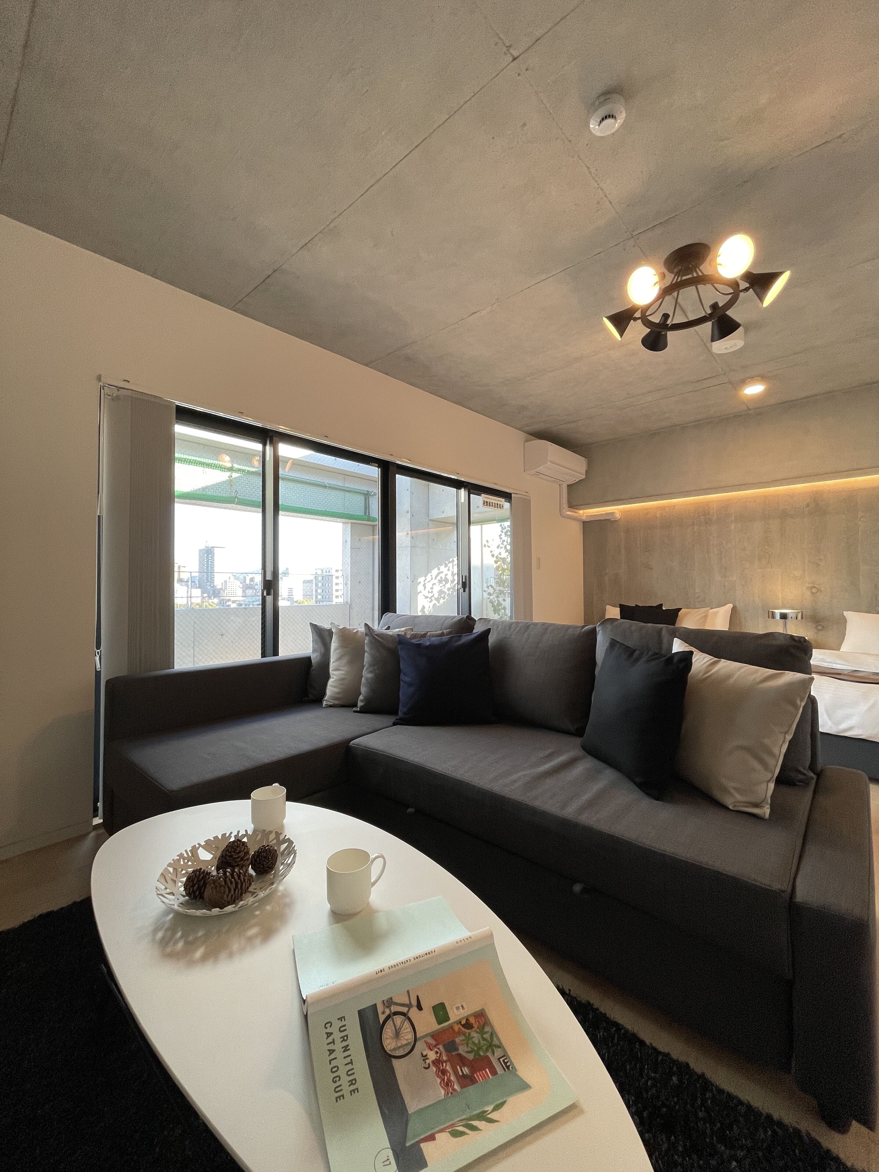 A modern hotel room with a grey sofa, a white coffee table, and a book titled 'Furniture Catalogue'.