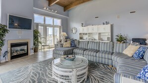Uma sala de estar com um amplo sofá modular, uma mesa de centro redonda, lareira e uma grande janela com vista.