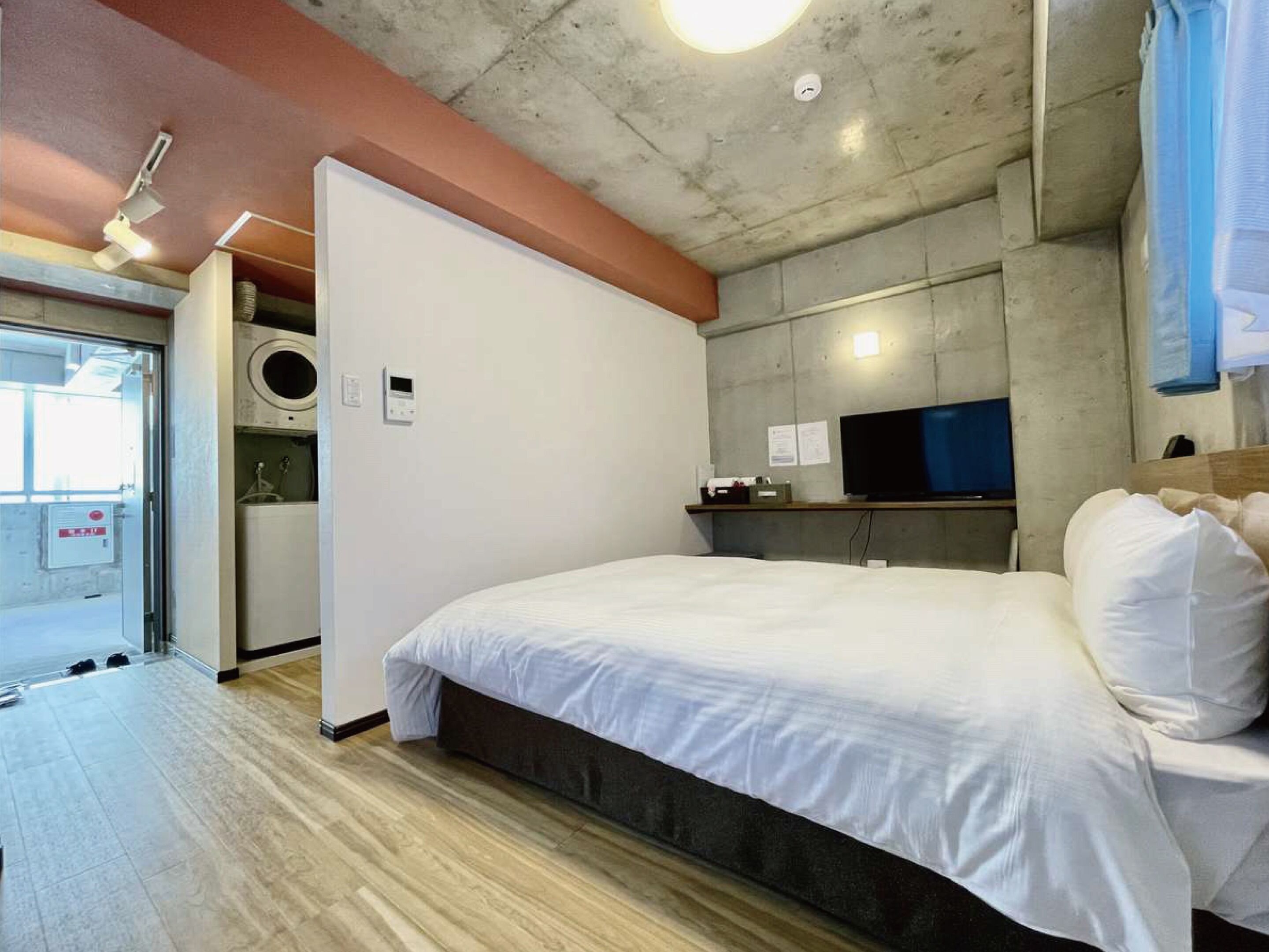 A modern hotel room with a large bed, a television, and a small kitchenette.