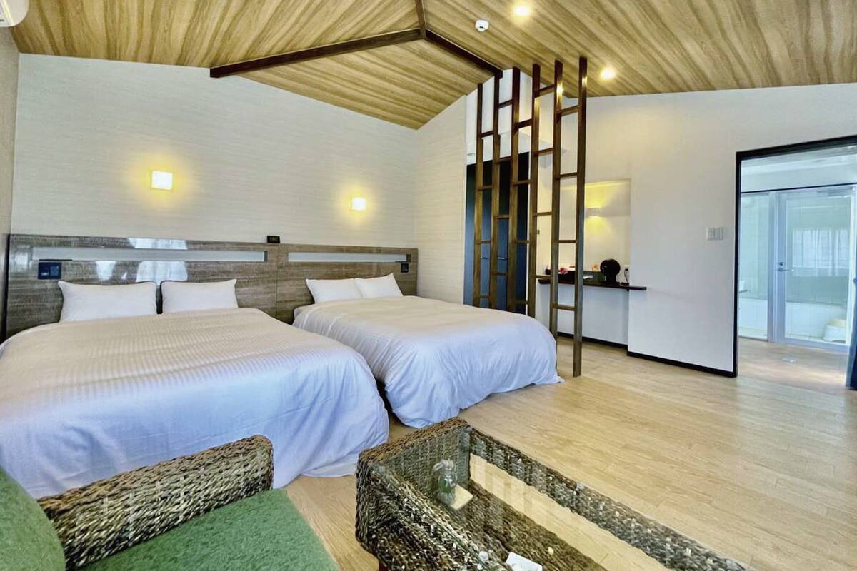 Habitación de hotel moderna con dos camas, techo de madera y vistas al exterior.