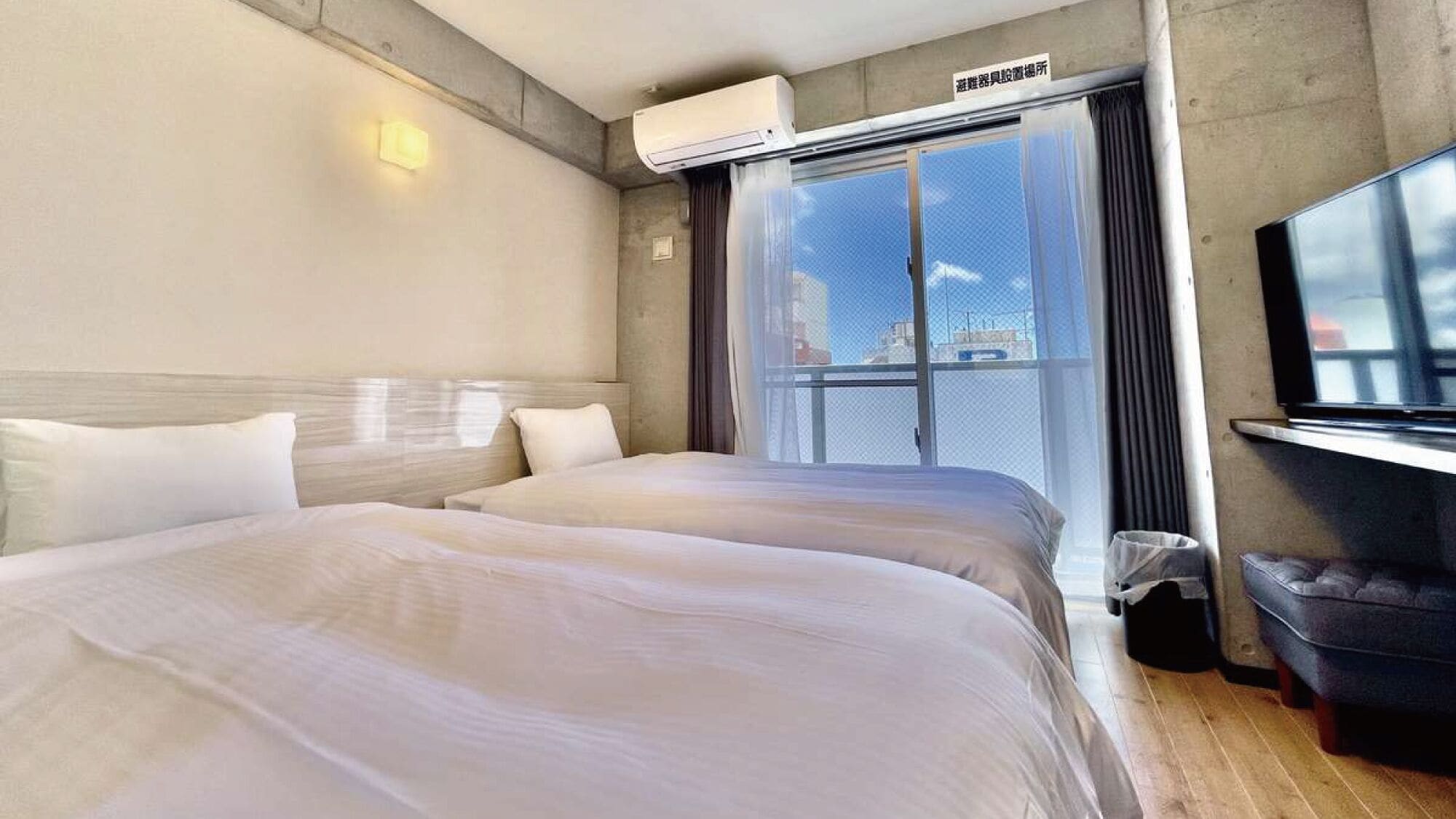 Een hotelkamer met een bed, een televisie, een airconditioning en een raam met uitzicht.