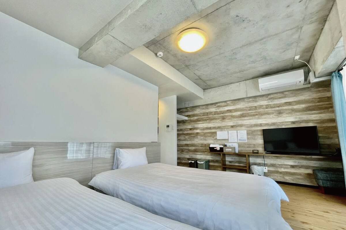 Una habitación de hotel moderna con dos camas, un televisor de pantalla plana montado en la pared y una pared decorativa de madera.