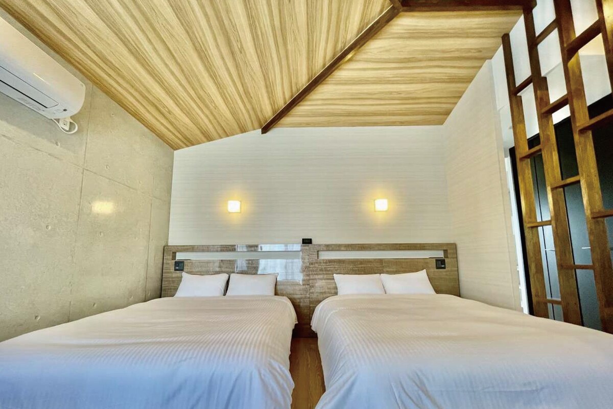 A hotel room with two beds, a wooden ceiling, and a window with a view.
