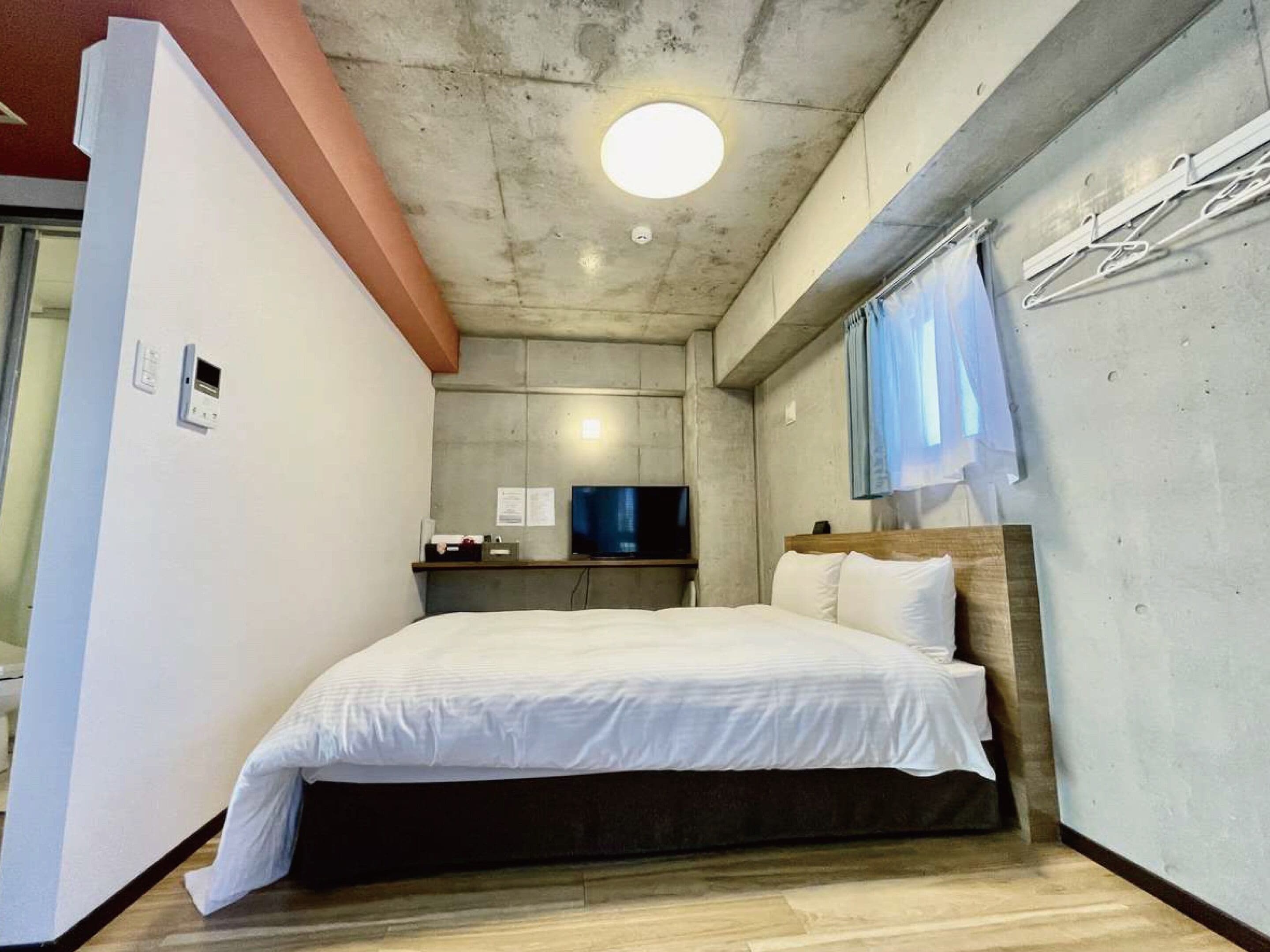 A hotel room with a bed, a television, a wall-mounted heater, and a window with curtains.