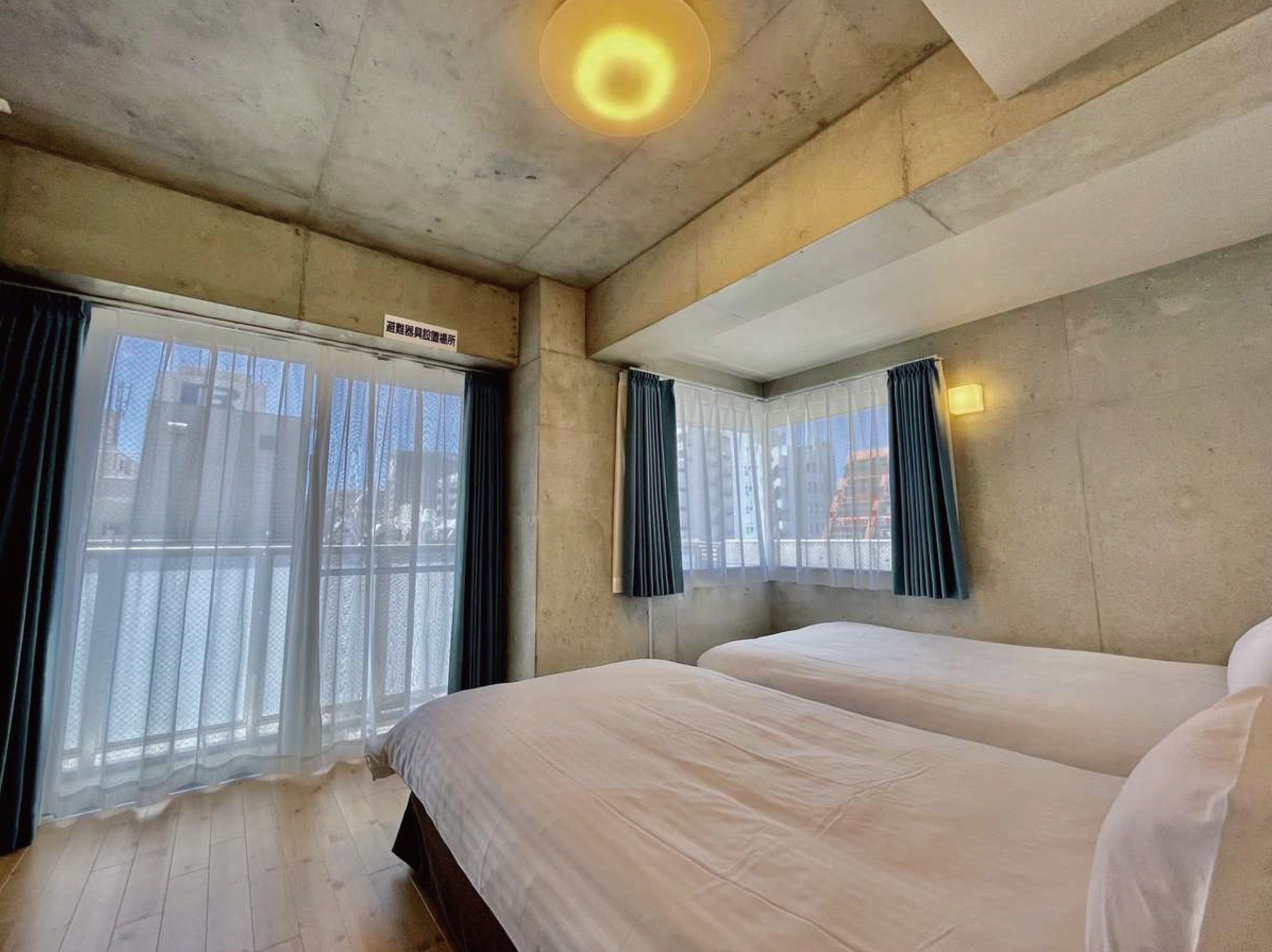 A hotel room with a large bed, a window with sheer curtains, and a ceiling light.