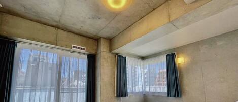 A hotel room with a large bed, a window with sheer curtains, and a ceiling light.