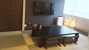A modern living room with a flat-screen TV mounted on the wall, a wooden dining table, and a tatami mat floor. - Kyoto Central Inn (Kyoto)