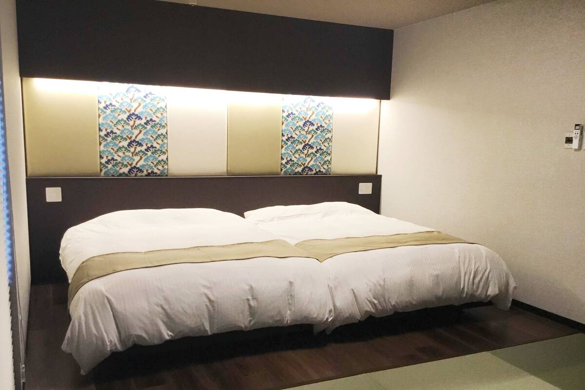 Ein ordentlich bezogenes Bett mit Kopfteil mit dekorativen Verzierungen, ein Nachttisch und eine wandmontierte Lampe.