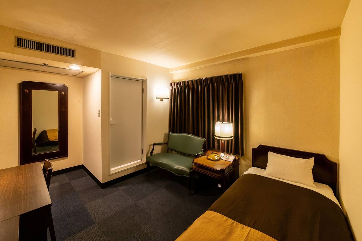 Ein Hotelzimmer mit Bett, Schreibtisch, Stuhl, Lampe und Spiegel.