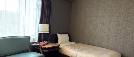 Una habitación de hotel con cama, escritorio con lámpara, silla y ventana con cortinas.