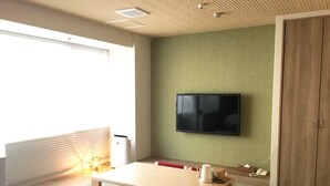 A room with a wooden table, red cushioned chairs, a flat-screen TV mounted on the wall, a window with blinds, and a door. - Kyoto Central Inn (Kyoto)