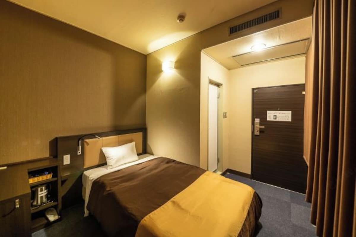 A hotel room with a bed, a bedside table, a wardrobe, and a door.