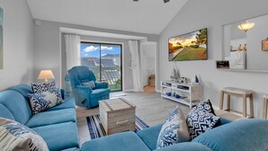 Un salon moderne comprenant un grand ensemble de canapés, un fauteuil bleu, une table basse en bois et un ventilateur de plafond.