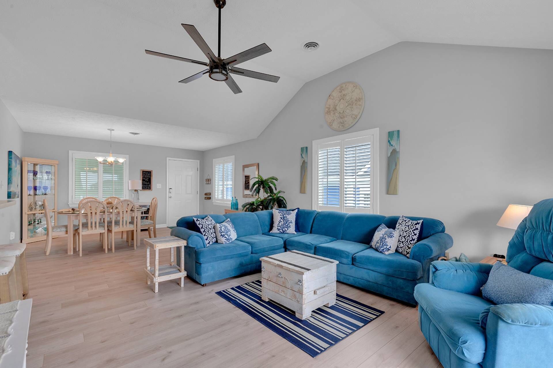 A spacious living room with a blue sectional sofa, a wooden coffee table, and a dining area with a wooden table and chairs.