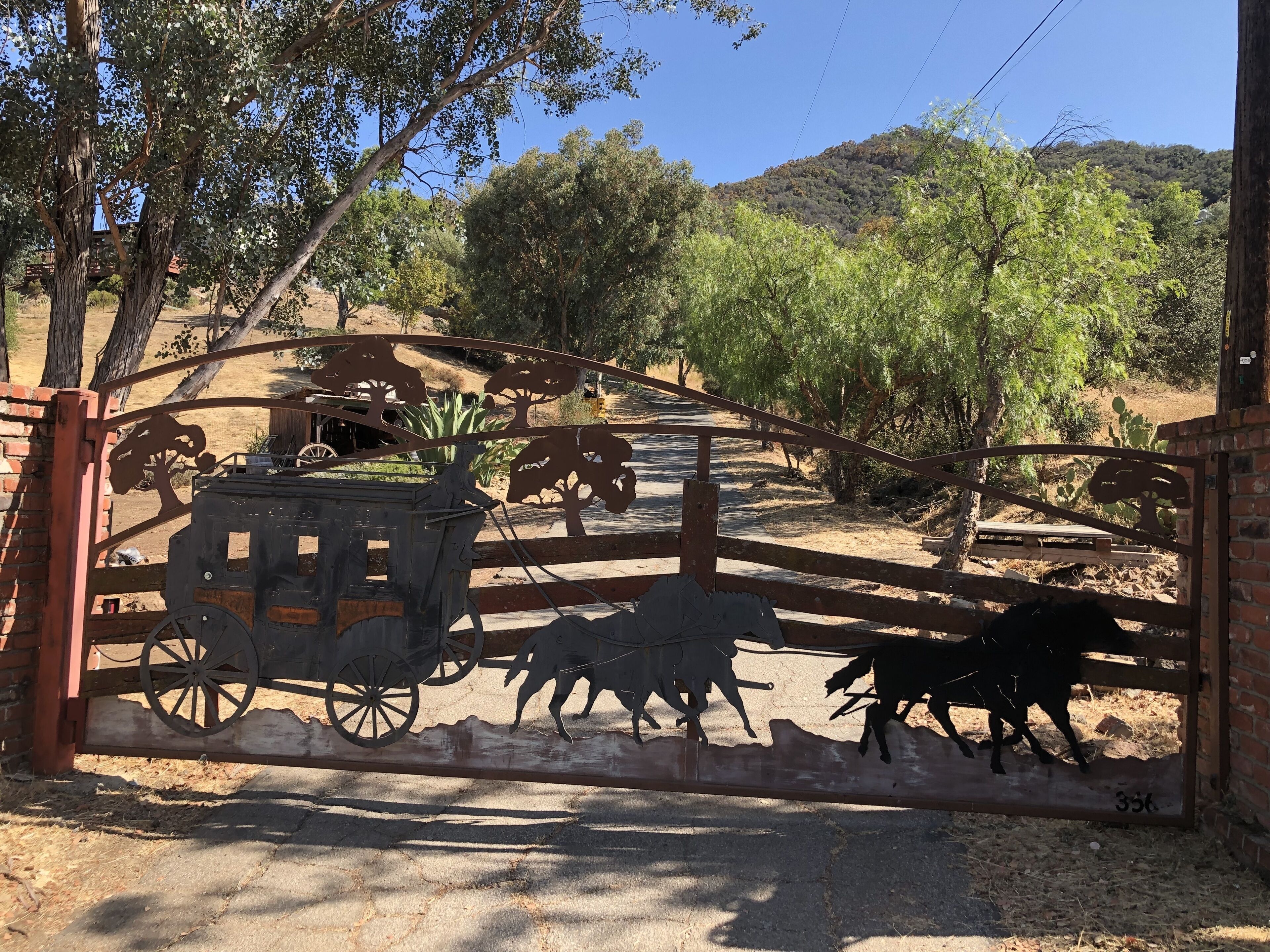 Una reja rústica con un carruaje de madera y siluetas de caballos, que da paso a un paisaje seco y montañoso.
