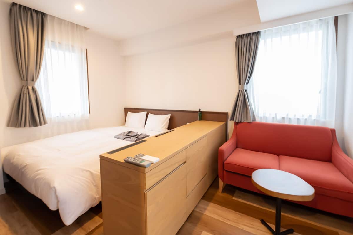 A hotel room with a bed, a wooden dresser, a red sofa, and a small round table.