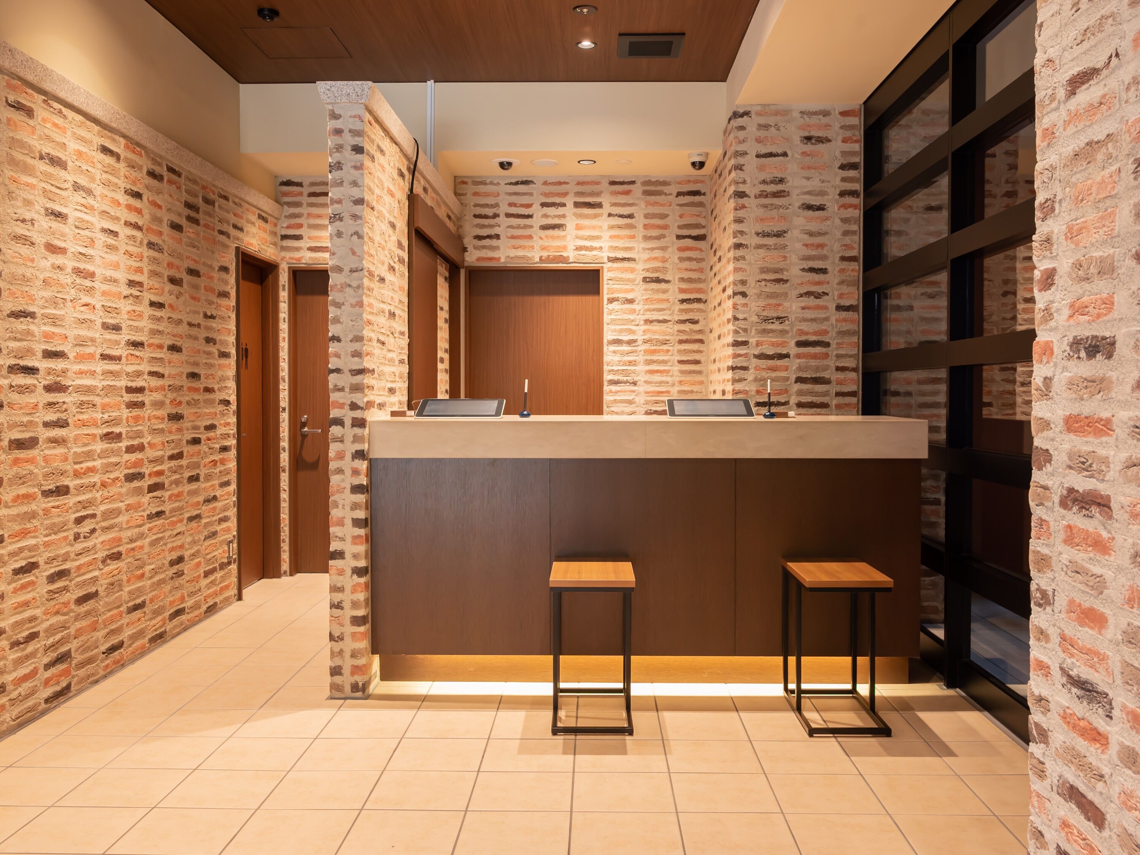 A modern interior with brick walls, a wooden reception desk, and two bar stools.