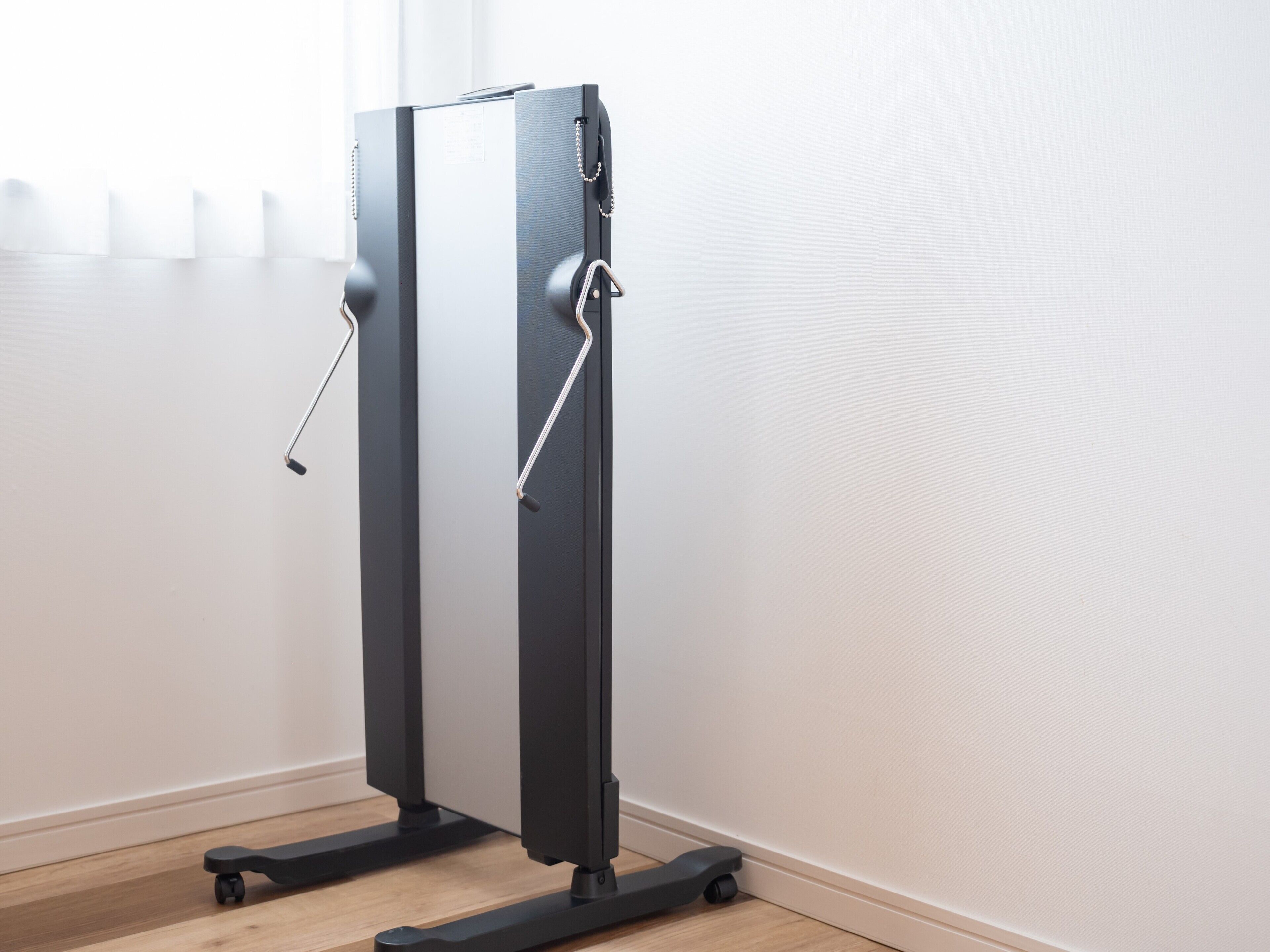 A piece of exercise equipment with a handle and a foot pedal, placed on a wooden floor against a white wall.