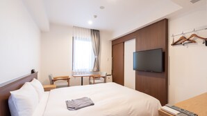 Ein Hotelzimmer mit Bett, Schreibtisch, Stuhl, Fernseher und Kleiderschrank.