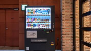 A vending machine with a variety of beverages and snacks, located in front of a brick wall and a door labeled "非常口".