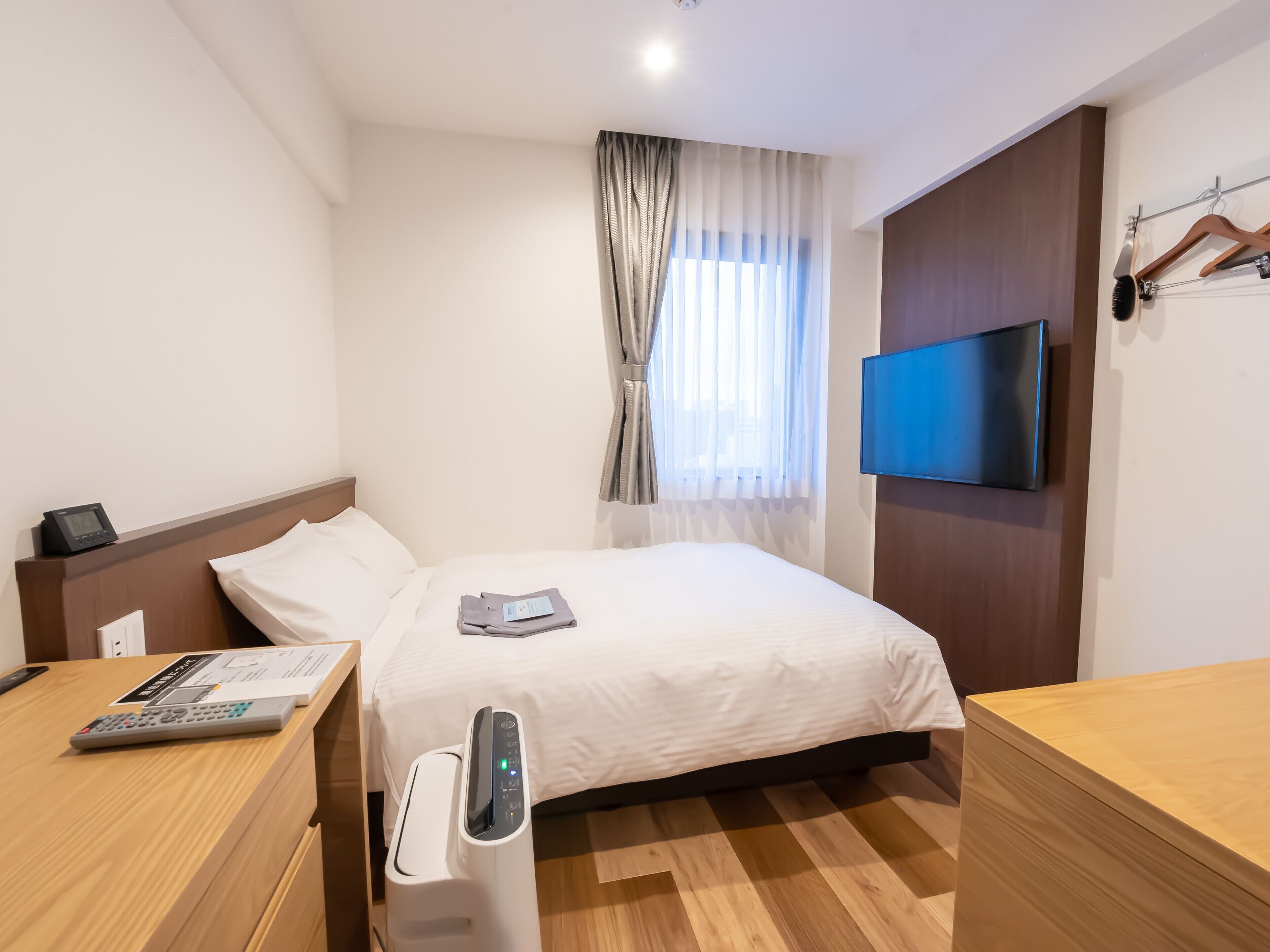 A hotel room with a bed, bedside table, TV, and a desk with a remote control.
