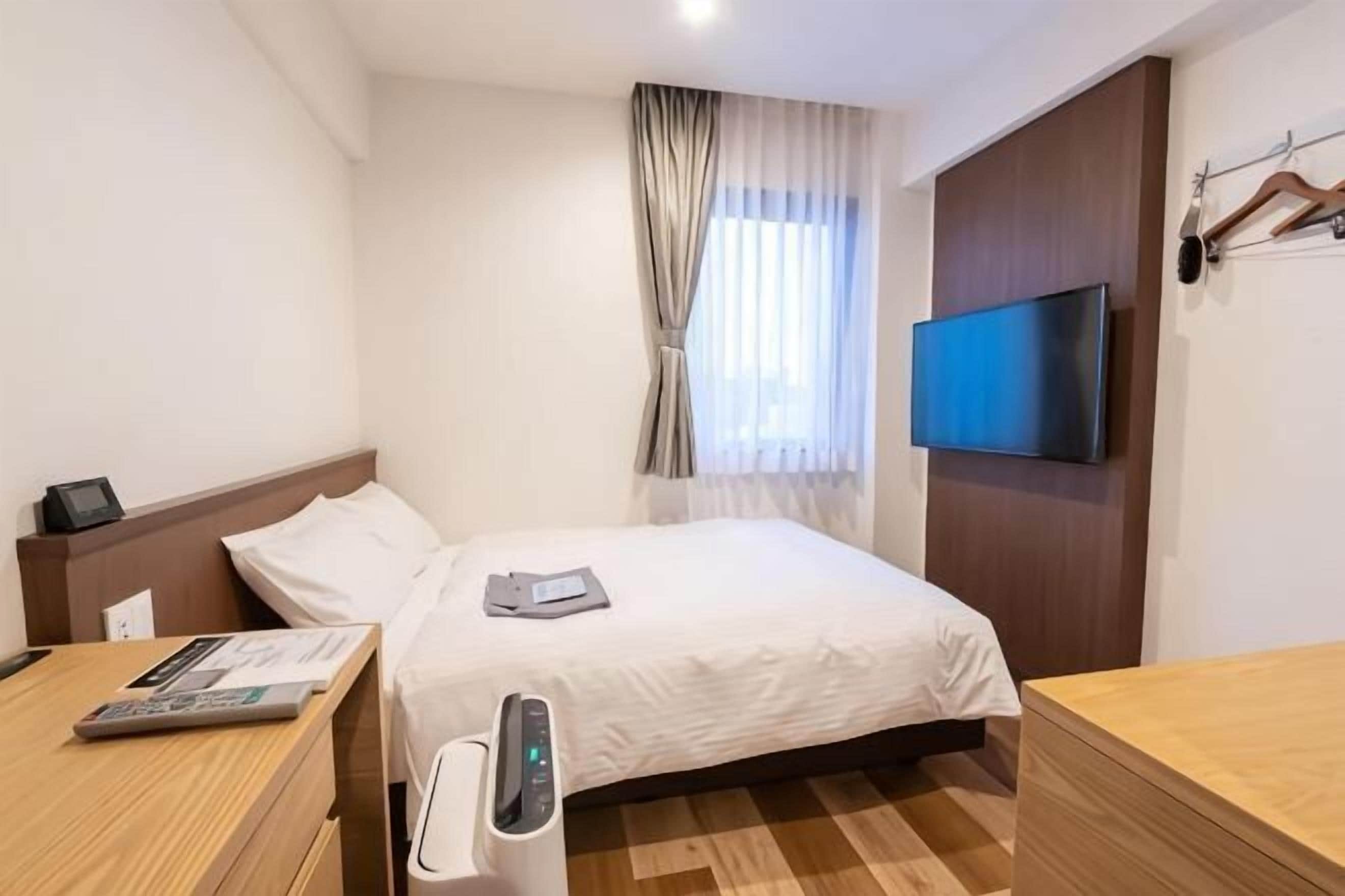 A hotel room with a bed, bedside table, TV, and a desk with a chair.