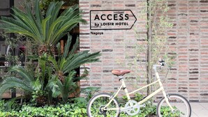 Ein Fahrrad vor einem Backsteinhaus mit einem Schild, auf dem steht: ACCESS by LOISIR HOTEL Nagoya.