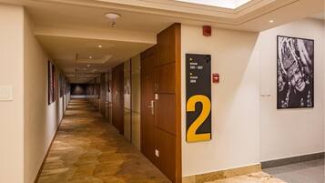 Um corredor de hotel com piso de carpete, portas de madeira e uma placa indicando os quartos 201 a 207 e 208.