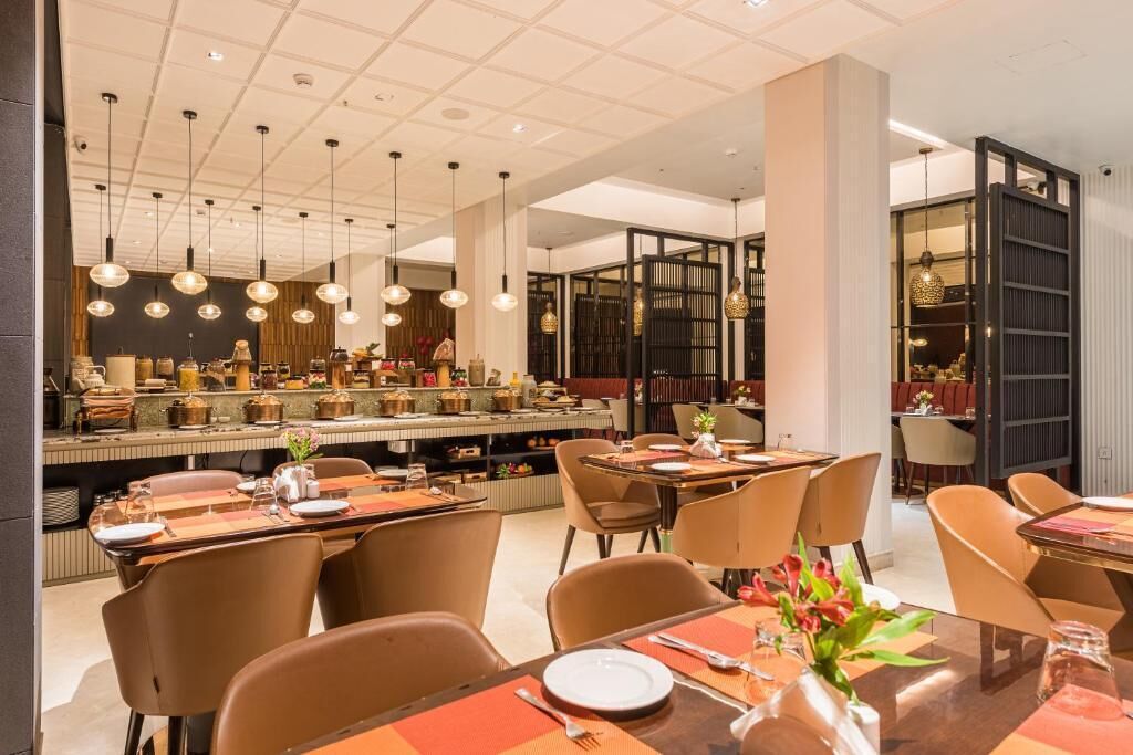A modern restaurant with multiple dining areas, a central bar, and hanging pendant lights.