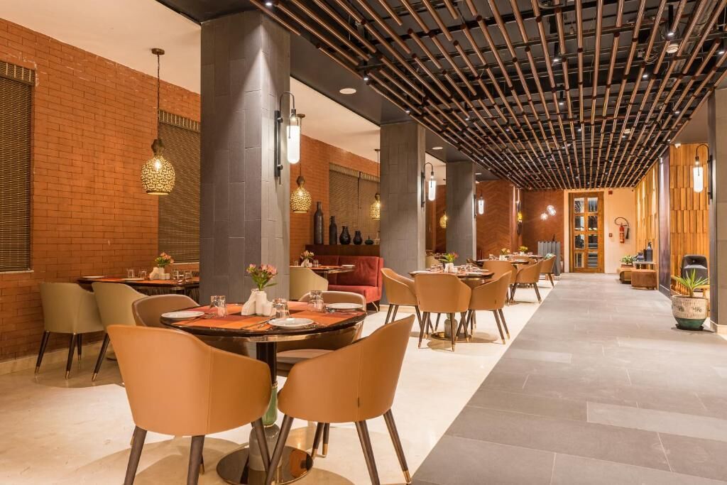 Een moderne eetruimte met bakstenen muren, houten balken en meerdere tafels en stoelen.