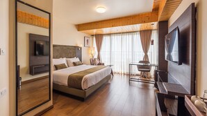 A modern hotel room with a large bed, a TV, a wooden ceiling, and a large window with curtains. - Udaan Himalayan Suites and Spa (Darjeeling)