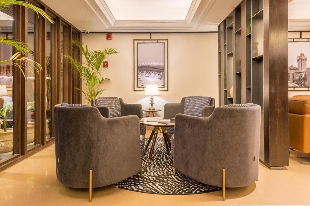 Un hall d’entrée avec deux fauteuils gris, une petite table ronde, une lampe et un tableau encadré au mur.