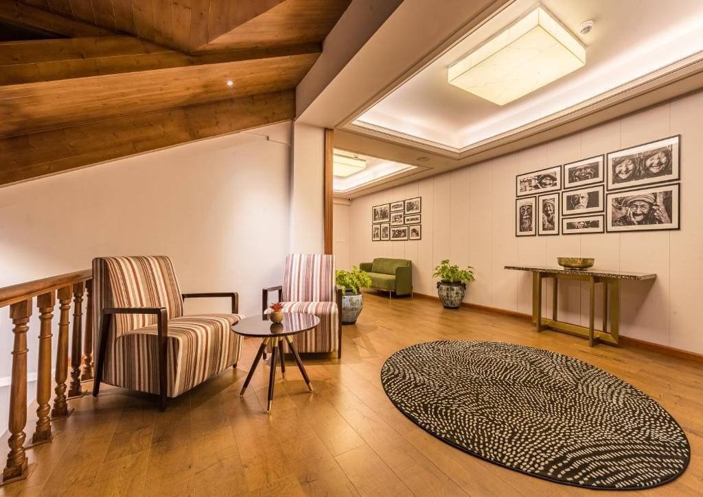 A spacious living room with a wooden staircase, a striped armchair, a green sofa, a round rug, and framed pictures on the wall.