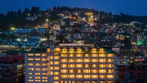 A multi-story hotel with numerous illuminated windows, surrounded by a densely populated hillside residential area. - Udaan Himalayan Suites and Spa (Darjeeling)