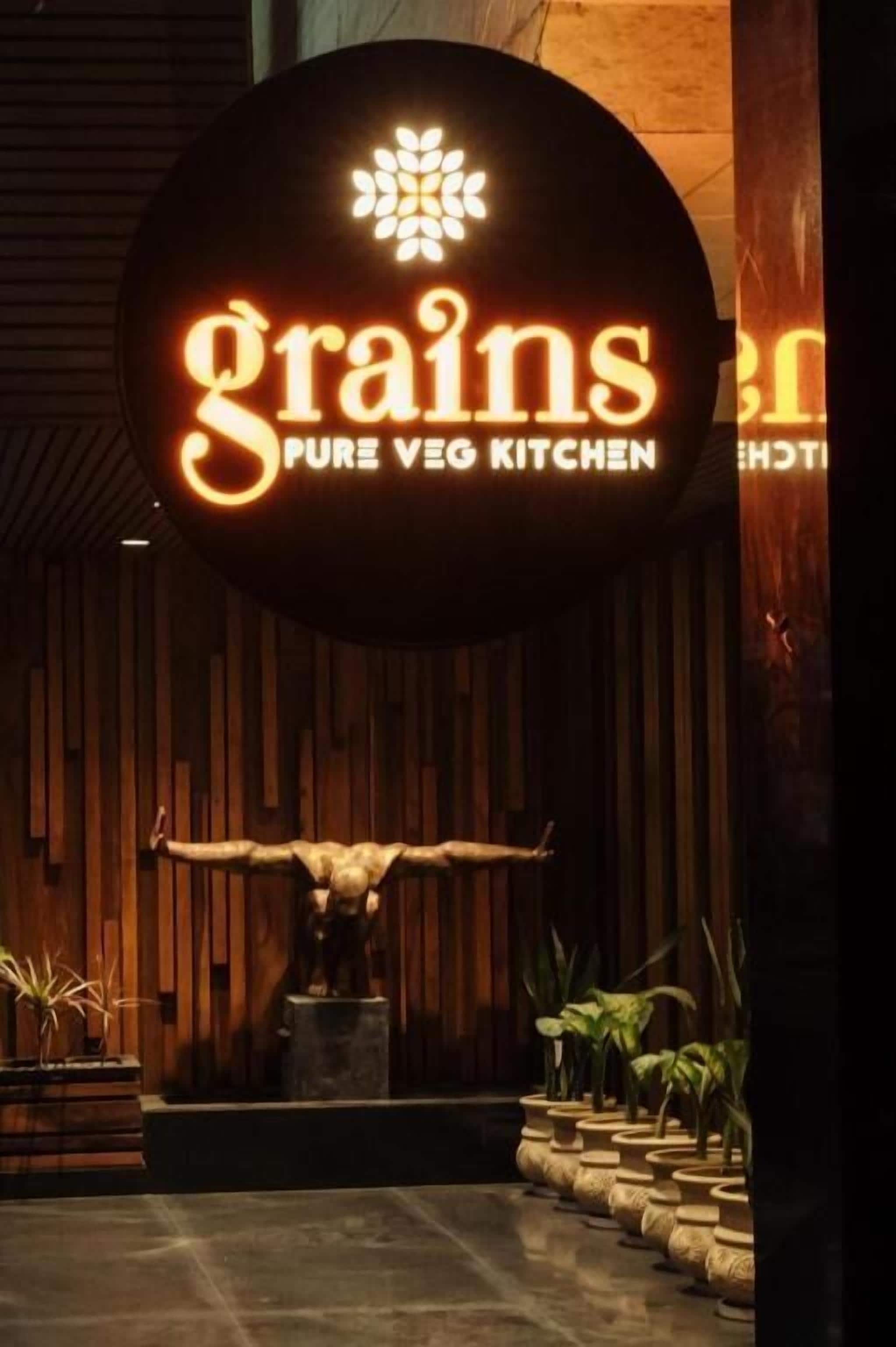 Een bord met de naam 'Grains Pure Veg Kitchen' en een decoratief beeld van een koeienhoofd ervoor.