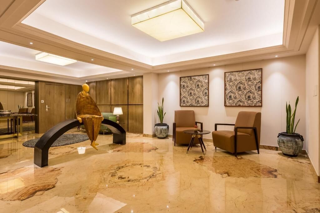 A lobby with a marble floor, a large chandelier, a sofa, two chairs, and two potted plants.