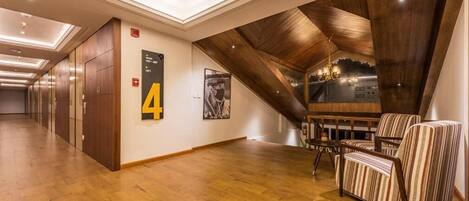 Un couloir d’hôtel avec un plancher en bois, une porte portant le numéro « 4 », un escalier et des fauteuils à rayures.