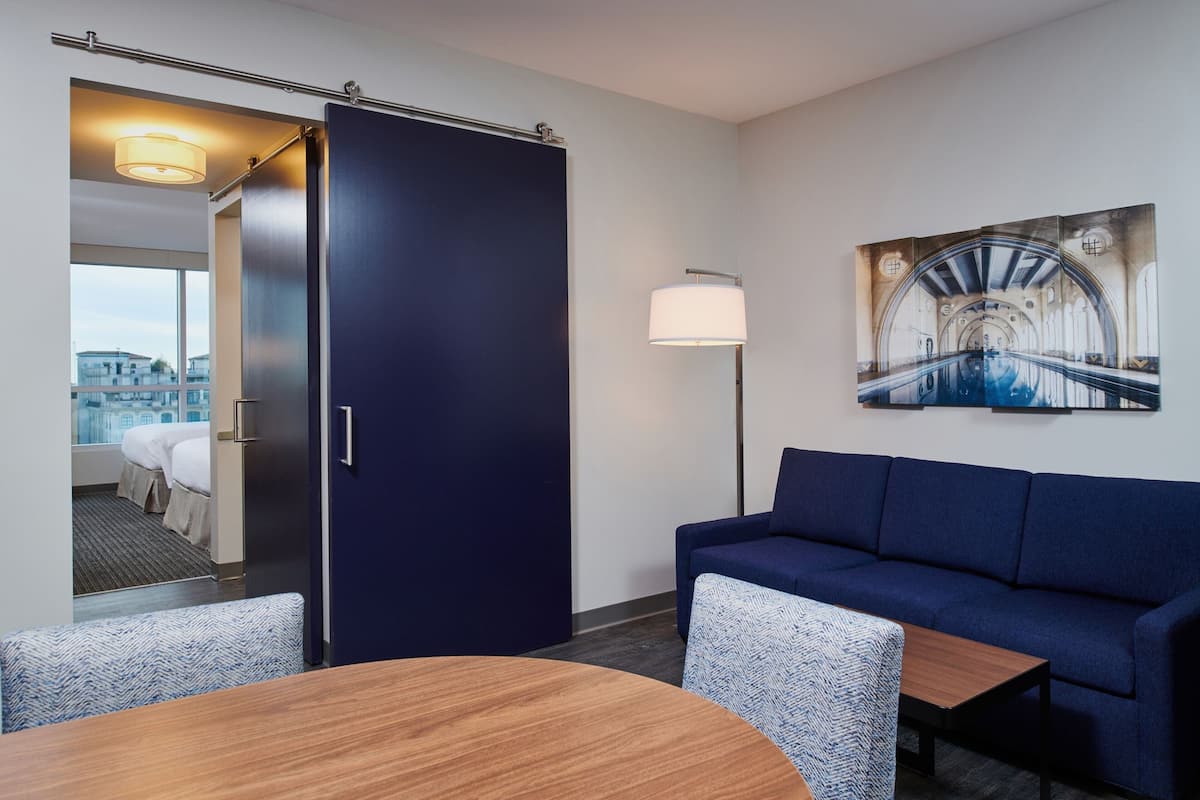 A hotel room with a large dark blue sliding door, a blue sofa, a round wooden table, and a floor lamp.
