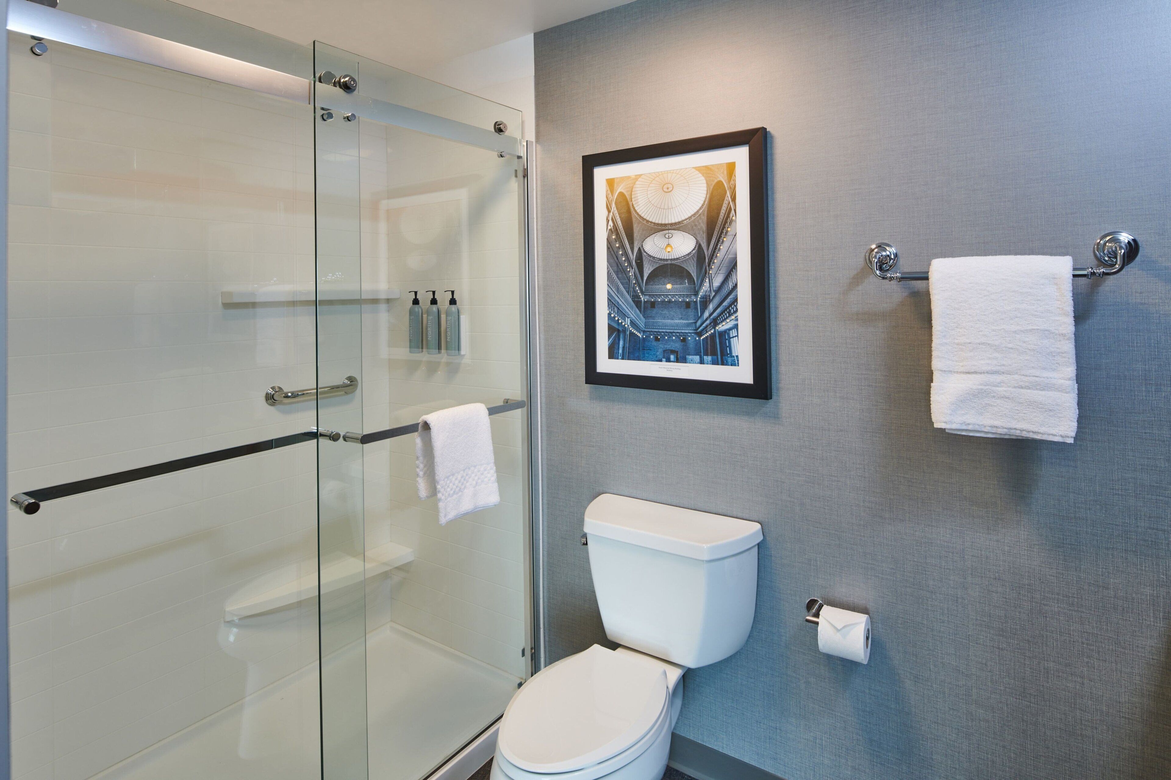 Une salle de bain moderne avec une douche à parois de verre, des toilettes blanches et un tableau encadré au mur.