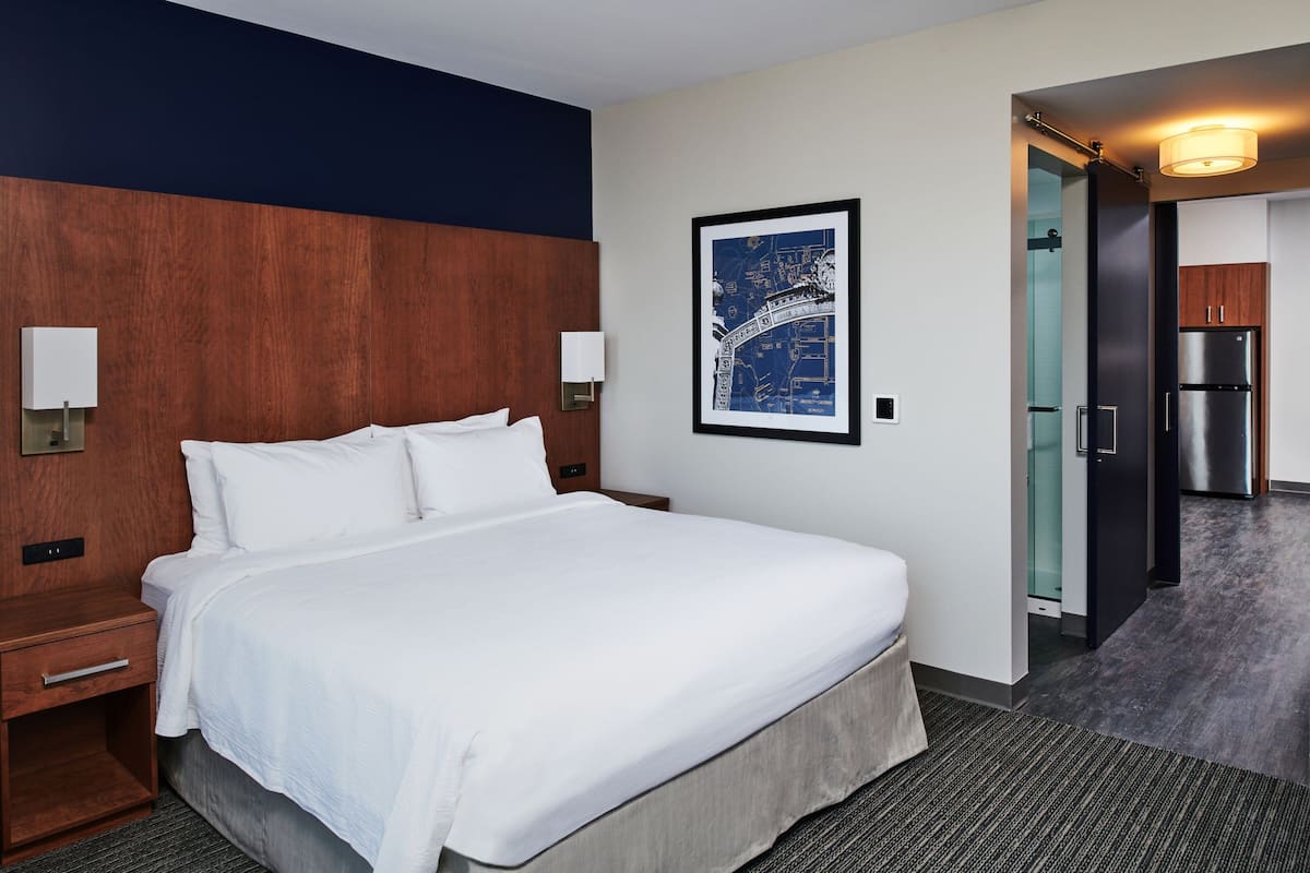 A hotel room with a large bed, a wooden headboard, a framed map on the wall, a minibar, and a refrigerator.