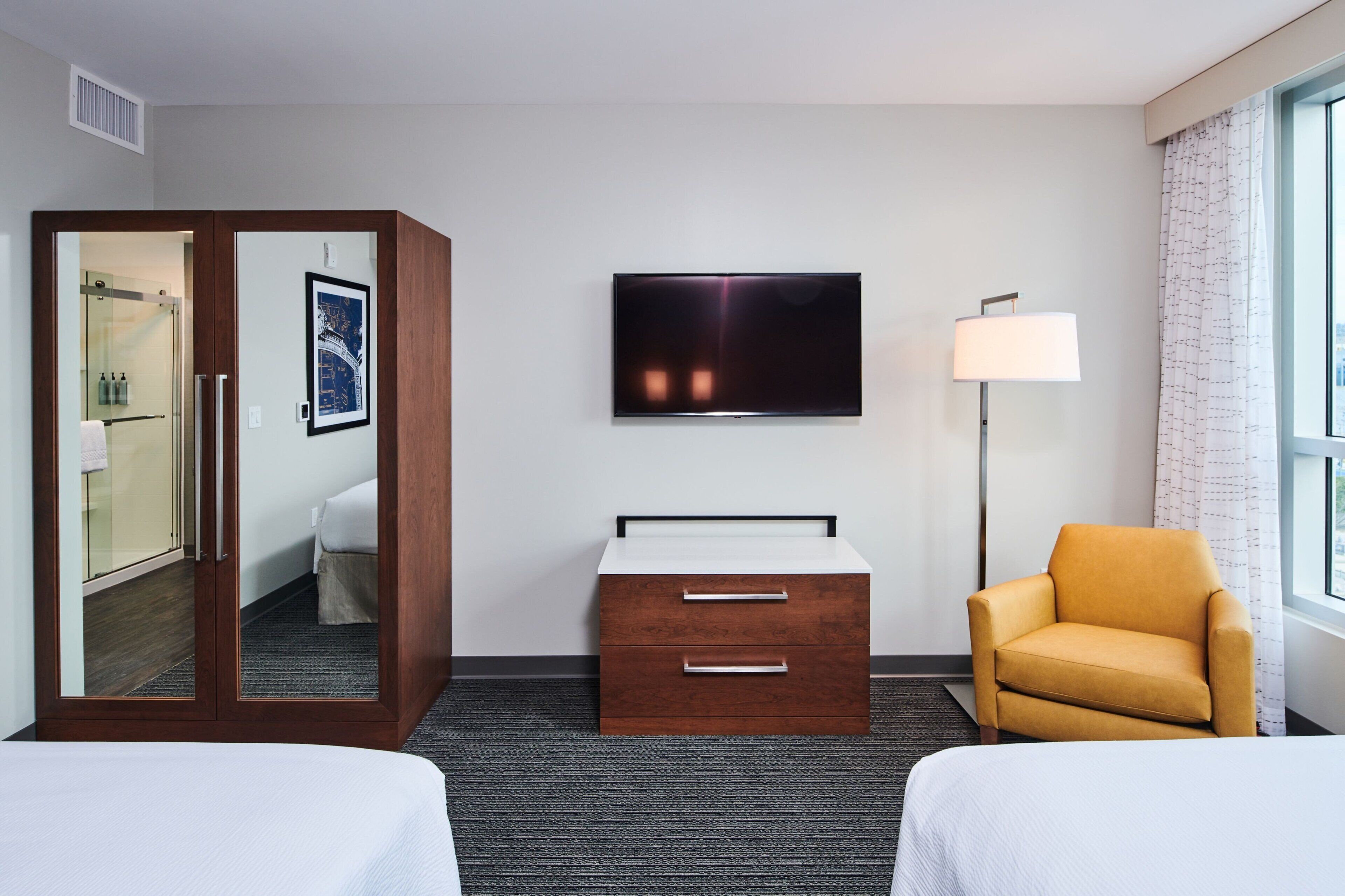 A hotel room with two beds, a TV, a desk with drawers, a chair, and a window with curtains.