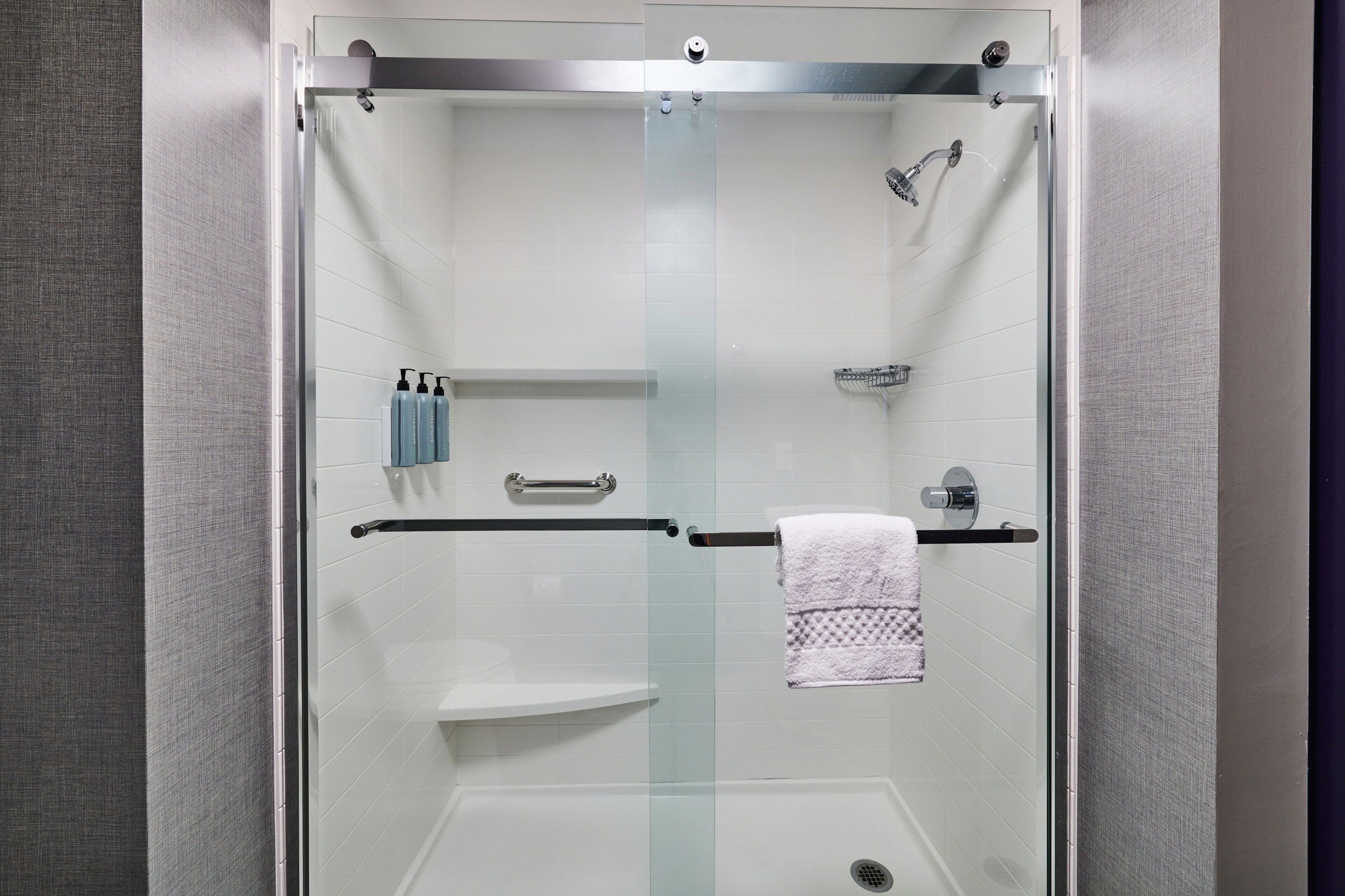 A modern shower with a glass door, a towel rack, and a shelf with toiletries.