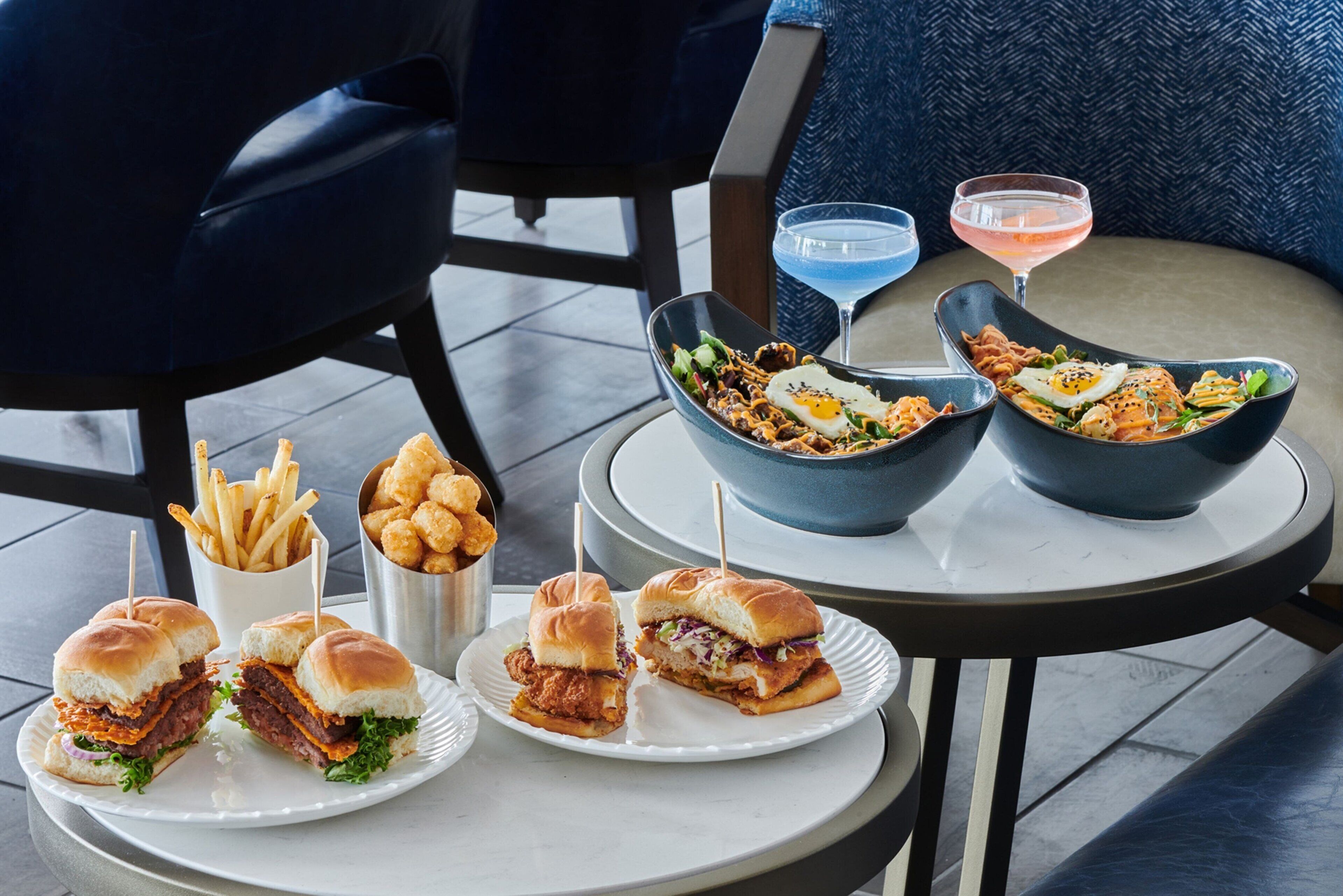 Ein Tisch mit Speisen, darunter Burger, Pommes und ein Salat, sowie zwei Getränke.