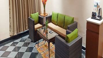 Una habitación con un sofá, dos sillones, una mesita de centro, una pequeña mesita auxiliar con un florero, una alfombra estampada y un minibar.