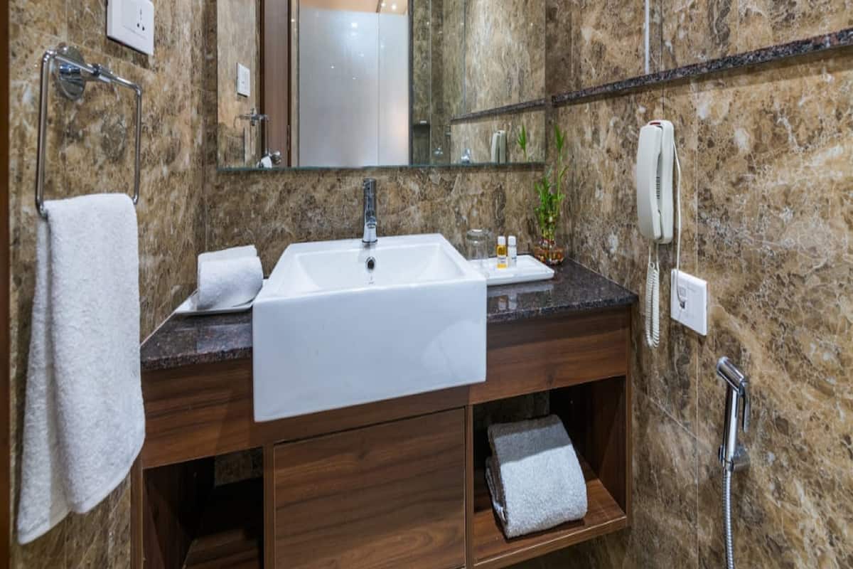 Un baño con pared de mármol, un lavabo, un espejo, un perchero para toallas, un teléfono y una ducha.