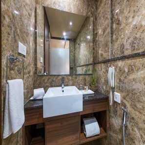 Une salle de bain avec un mur en marbre, un lavabo, un miroir, un porte-serviettes, un téléphone et une douche.