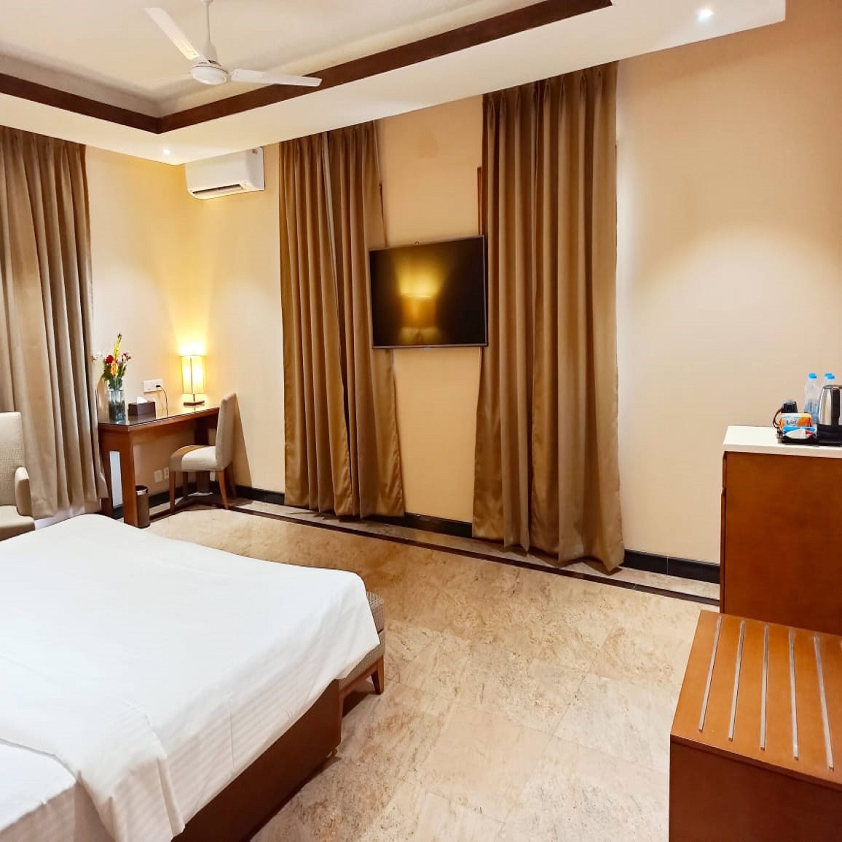 A hotel room with a bed, a desk, a chair, a TV, and curtains.