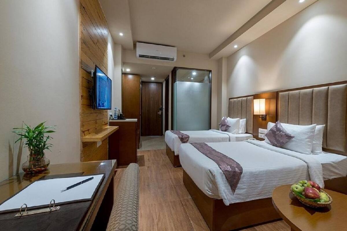 Habitación de hotel con dos camas, un escritorio con una libreta, una planta y una cesta de frutas.