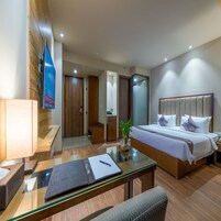 Una habitación de hotel moderna con una cama grande, un escritorio con una computadora portátil, una mesa de vidrio y una planta pequeña.