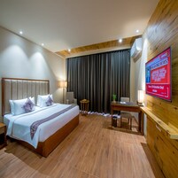 Habitación de hotel con cama, mesitas de noche, escritorio, silla, televisor y un amplio ventanal con cortinas.